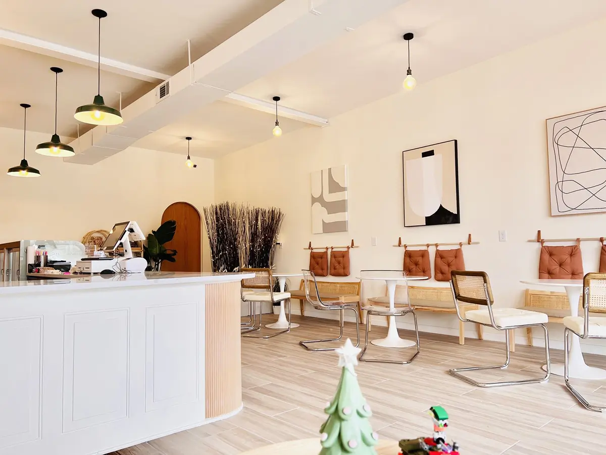A bright cafe interior with a white counter, pendant lights, modern art, mixed chairs, and small Christmas decor.